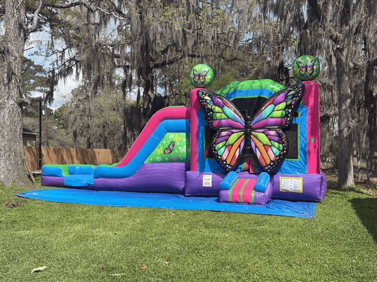 Colorful inflatable bounce house and slide combo set up outdoors on a grassy lawn with cartoon-style character artwork on the front.